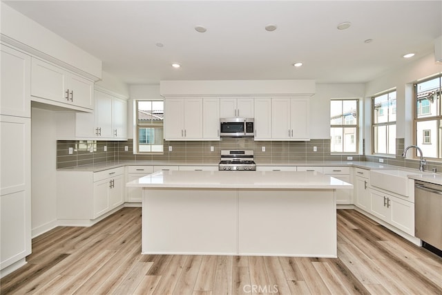 kitchen featuring stainless steel appliances, a kitchen island, light wood-type flooring, and white cabinetry