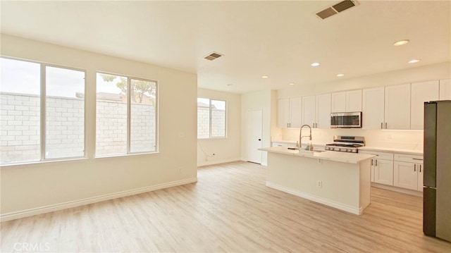 kitchen featuring appliances with stainless steel finishes, a center island with sink, white cabinetry, and light hardwood / wood-style floors