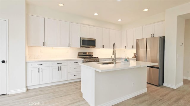 kitchen featuring a kitchen island with sink, white cabinets, sink, light hardwood / wood-style flooring, and stainless steel appliances