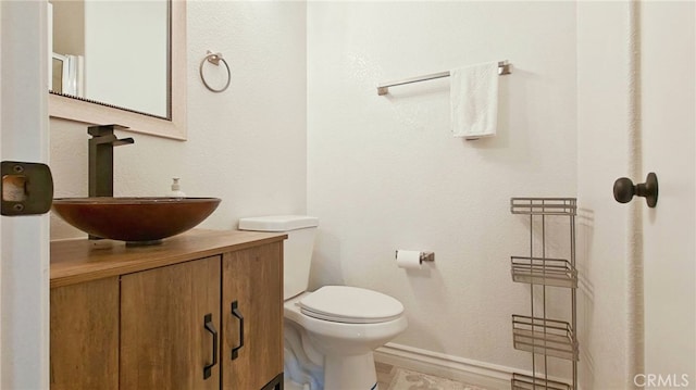 half bathroom featuring toilet, vanity, and baseboards