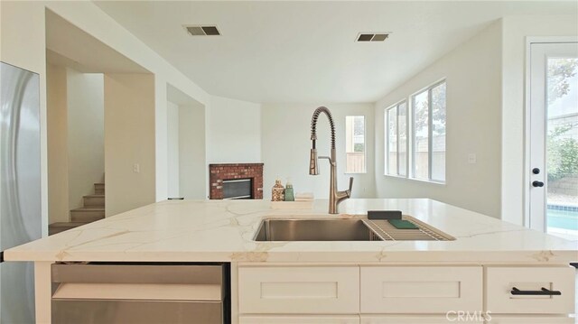 kitchen featuring light stone countertops, sink, stainless steel fridge, a fireplace, and white cabinets