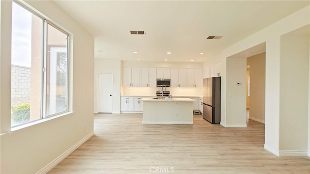 kitchen featuring light wood-type flooring, stainless steel appliances, white cabinetry, and a kitchen island with sink