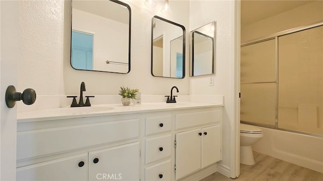 full bathroom featuring shower / bath combination with glass door, vanity, hardwood / wood-style flooring, and toilet