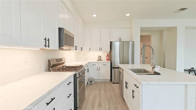 kitchen with light stone counters, an island with sink, light wood-style flooring, stainless steel appliances, and a sink