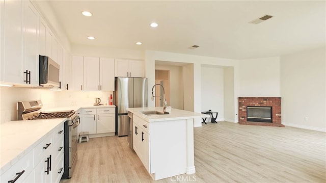 kitchen with light wood-type flooring, stainless steel appliances, sink, white cabinetry, and an island with sink