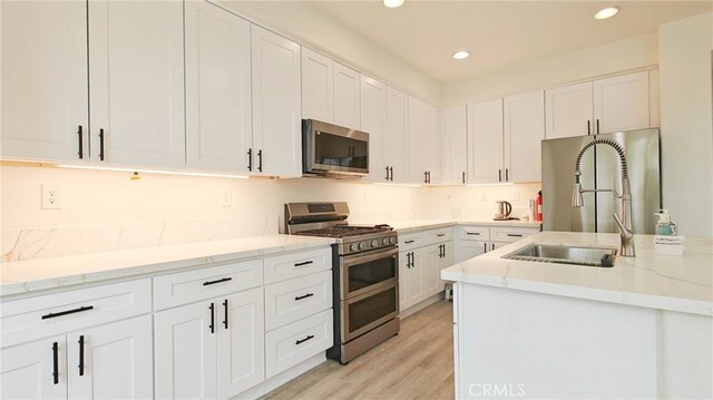 kitchen featuring white cabinets, sink, light stone countertops, light hardwood / wood-style floors, and stainless steel appliances