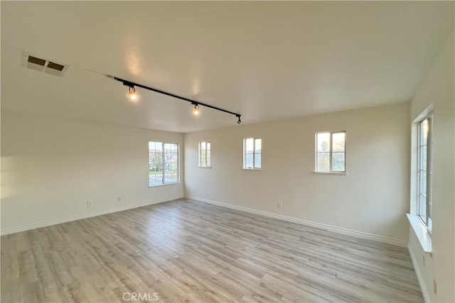 empty room featuring light hardwood / wood-style floors, rail lighting, and a wealth of natural light