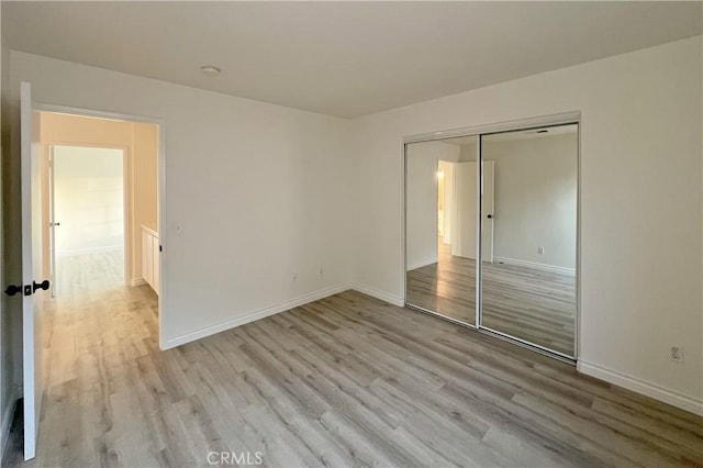 unfurnished bedroom with a closet, light wood finished floors, and baseboards