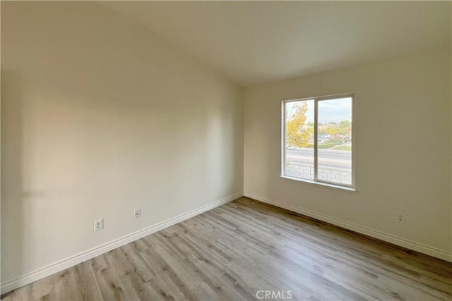 unfurnished room featuring vaulted ceiling, wood finished floors, and baseboards