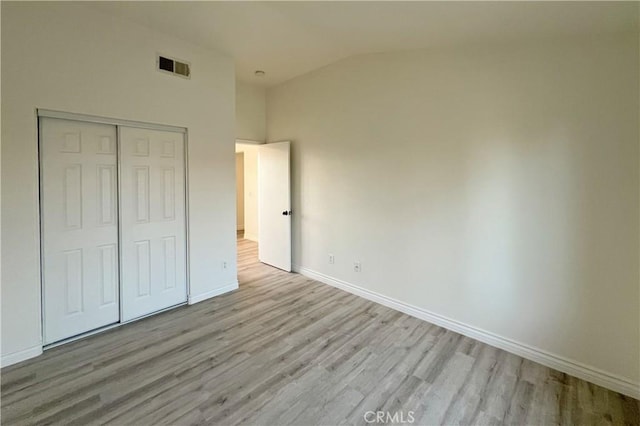 unfurnished bedroom featuring wood finished floors, visible vents, vaulted ceiling, a closet, and baseboards