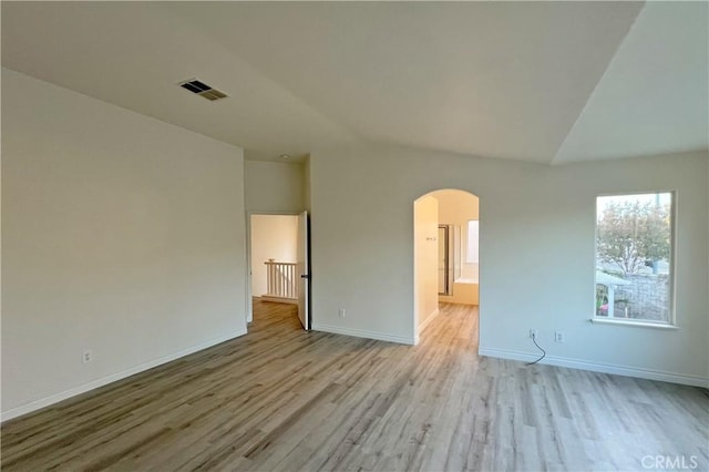 empty room featuring visible vents, baseboards, arched walkways, wood finished floors, and lofted ceiling