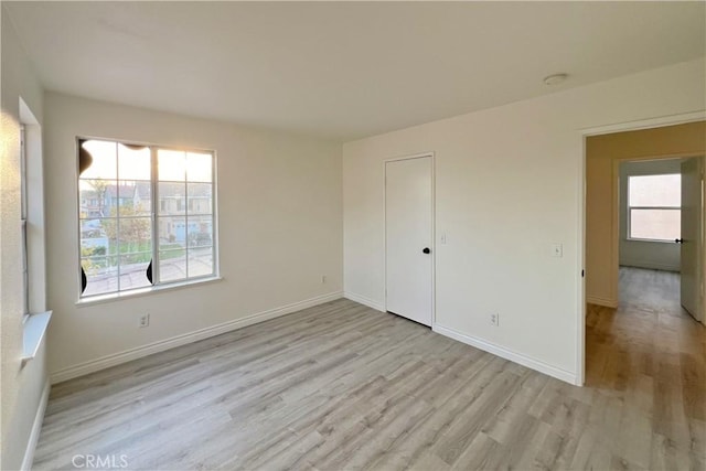 unfurnished bedroom featuring light wood-type flooring, a closet, and multiple windows