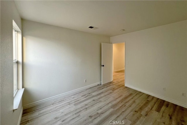 spare room featuring light wood-style floors, baseboards, visible vents, and plenty of natural light