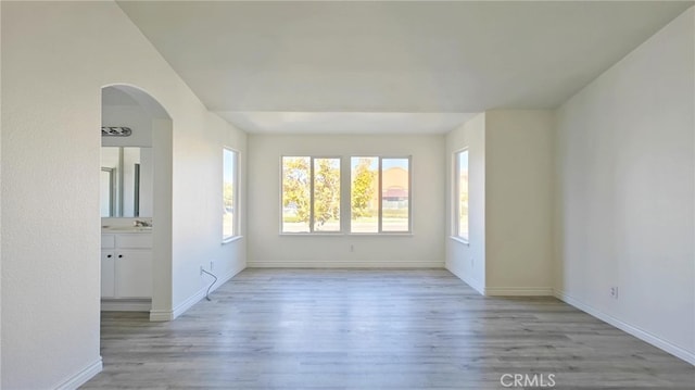 unfurnished room featuring arched walkways, a sink, light wood-type flooring, and baseboards