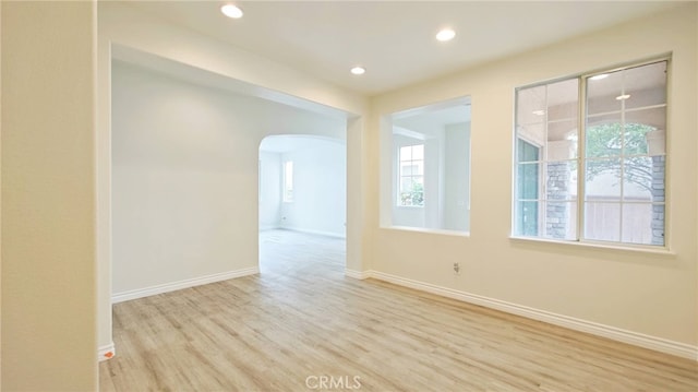 unfurnished room featuring recessed lighting, arched walkways, wood finished floors, and baseboards