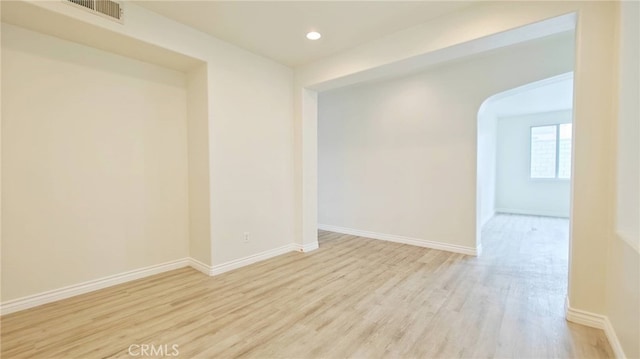 empty room with arched walkways, visible vents, recessed lighting, wood finished floors, and baseboards