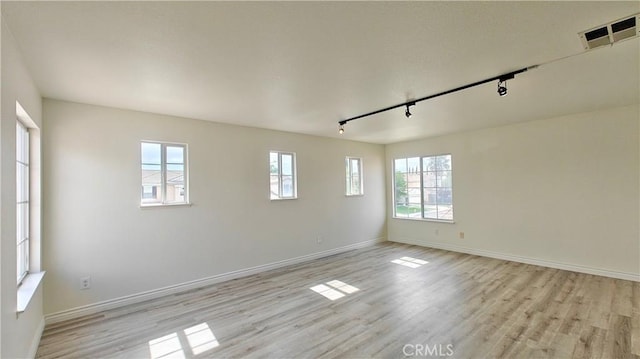 empty room featuring rail lighting, light wood finished floors, baseboards, and visible vents