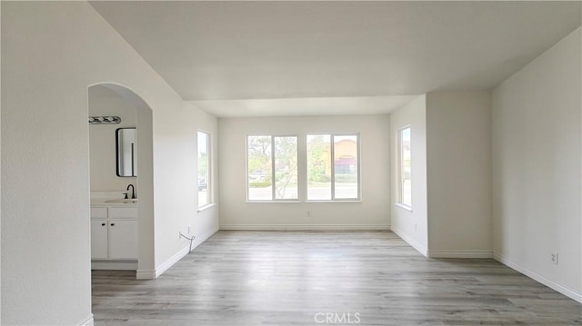 spare room with light wood-style flooring, arched walkways, a sink, and baseboards