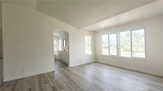 spare room with a sink, light wood-style floors, arched walkways, baseboards, and lofted ceiling