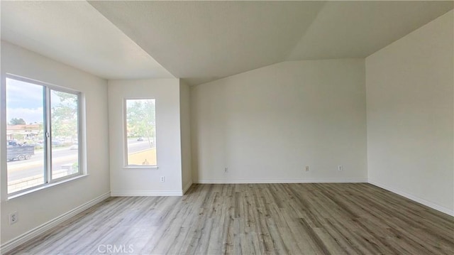 spare room with light wood-style flooring, baseboards, and lofted ceiling