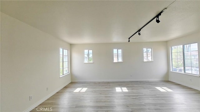 spare room featuring light wood-style flooring, baseboards, and rail lighting