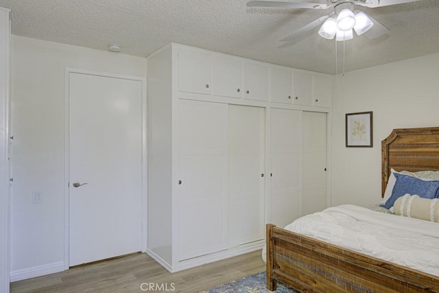 bedroom with ceiling fan, a closet, light hardwood / wood-style floors, and a textured ceiling