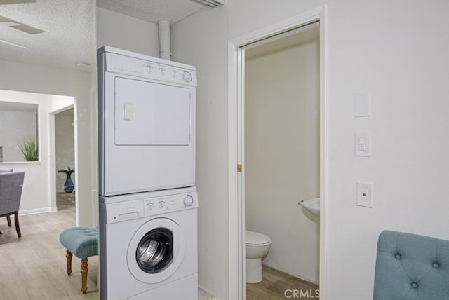 laundry area with a textured ceiling, light wood-type flooring, and stacked washer / dryer