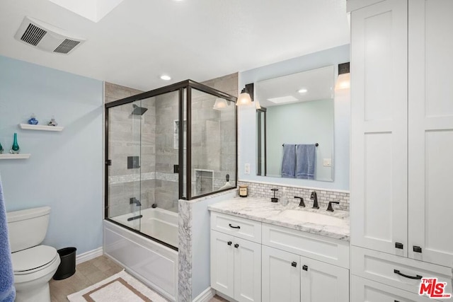 full bathroom with tile patterned flooring, toilet, shower / bath combination with glass door, decorative backsplash, and vanity