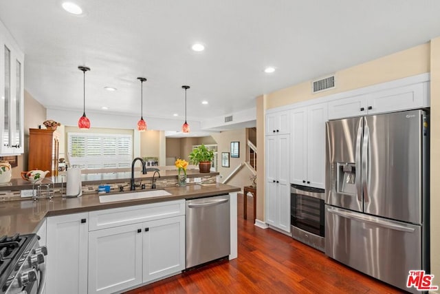 kitchen featuring appliances with stainless steel finishes, dark hardwood / wood-style flooring, sink, white cabinetry, and hanging light fixtures