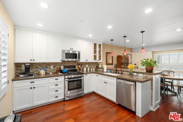 kitchen with kitchen peninsula, appliances with stainless steel finishes, sink, dark hardwood / wood-style floors, and hanging light fixtures