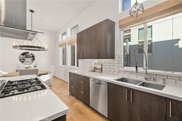 kitchen with stainless steel appliances, backsplash, sink, decorative light fixtures, and light wood-type flooring