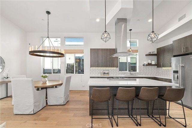 kitchen with high end refrigerator, dark brown cabinets, a kitchen island, island range hood, and light hardwood / wood-style floors