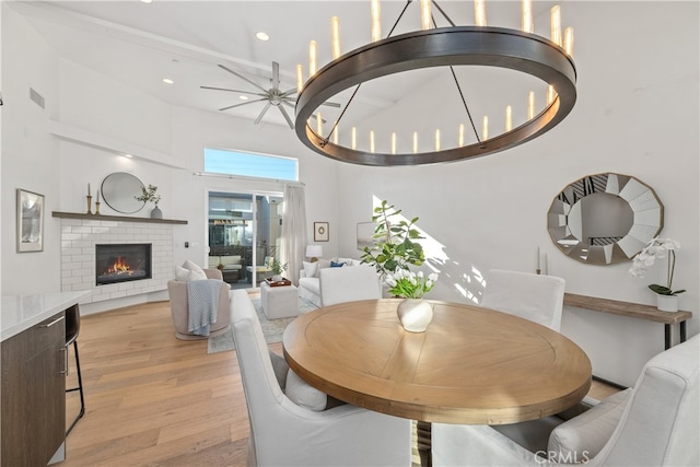 dining room with a brick fireplace, light wood-type flooring, and a high ceiling