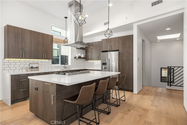 kitchen featuring high end refrigerator, hanging light fixtures, a center island, a kitchen bar, and light wood-type flooring