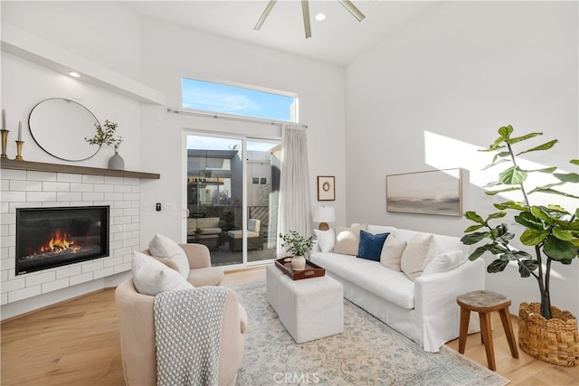 living room featuring a towering ceiling, a brick fireplace, light wood-type flooring, and ceiling fan