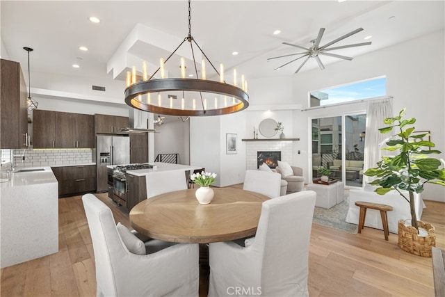 dining room with a brick fireplace, sink, light wood-type flooring, and ceiling fan with notable chandelier