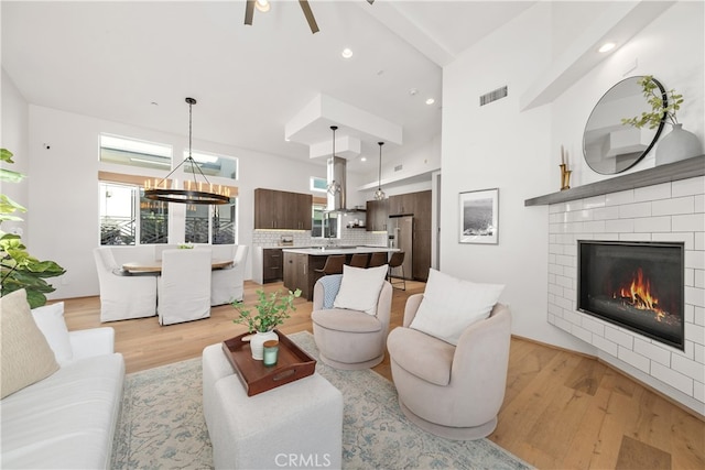 living room with sink, ceiling fan with notable chandelier, a fireplace, and light hardwood / wood-style floors