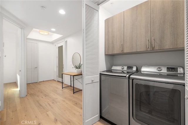 laundry area with washing machine and clothes dryer, light wood-type flooring, and cabinets