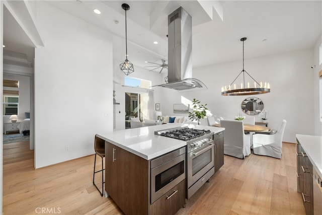 kitchen with island range hood, a center island, stainless steel appliances, pendant lighting, and light hardwood / wood-style flooring