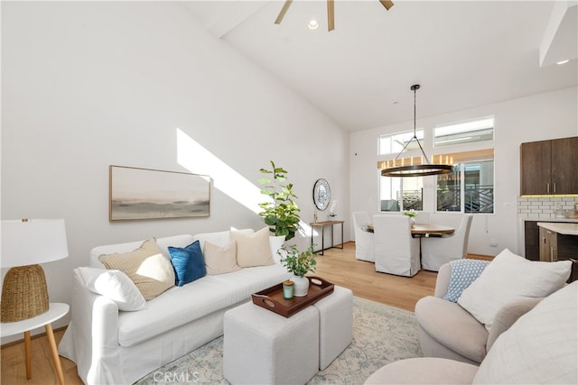 living room featuring high vaulted ceiling, light hardwood / wood-style flooring, and ceiling fan with notable chandelier