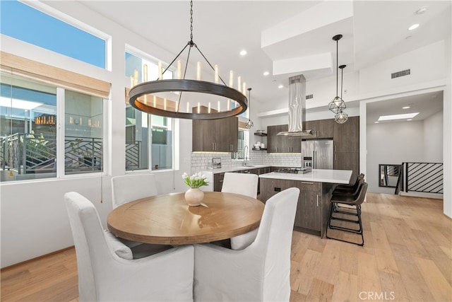 dining room with sink, lofted ceiling, light hardwood / wood-style flooring, and an inviting chandelier