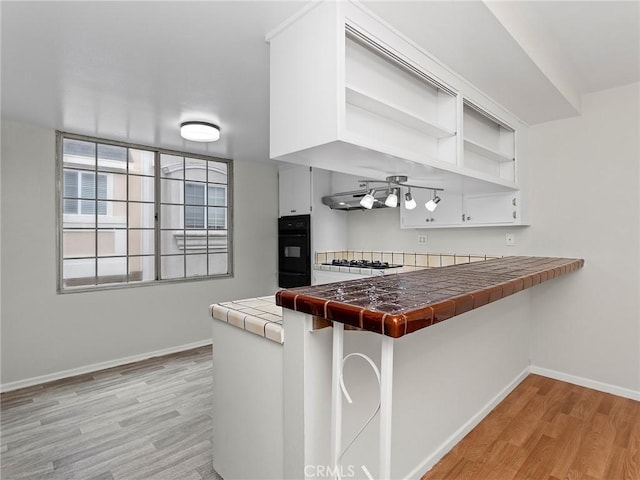 kitchen featuring tile countertops, kitchen peninsula, light wood-type flooring, white cabinetry, and gas cooktop