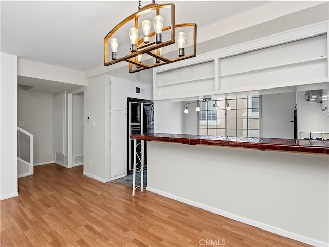 interior space with hanging light fixtures, light wood-type flooring, tile counters, kitchen peninsula, and a chandelier