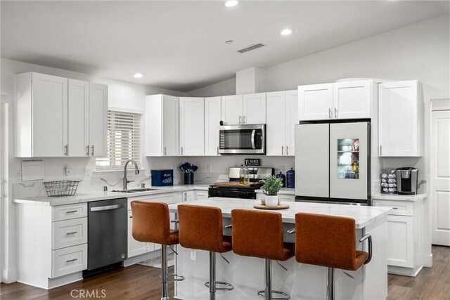 kitchen with stainless steel appliances, vaulted ceiling, sink, white cabinets, and a kitchen island