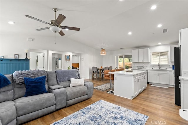 living room featuring ceiling fan, sink, vaulted ceiling, and light wood-type flooring