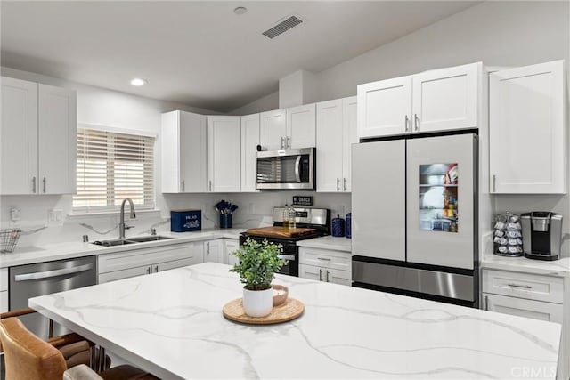 kitchen with a kitchen breakfast bar, stainless steel appliances, vaulted ceiling, sink, and white cabinetry