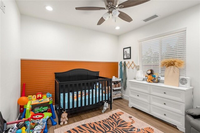 bedroom with ceiling fan, a crib, and light hardwood / wood-style flooring