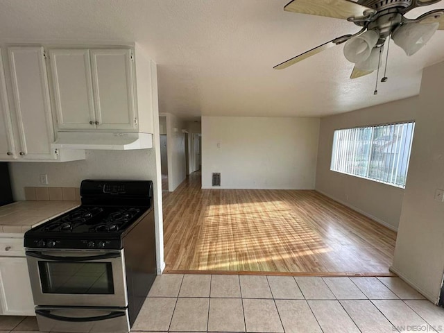 kitchen with stainless steel gas range oven, white cabinets, light wood-type flooring, and ceiling fan