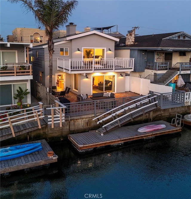 back house at dusk featuring a water view and a balcony