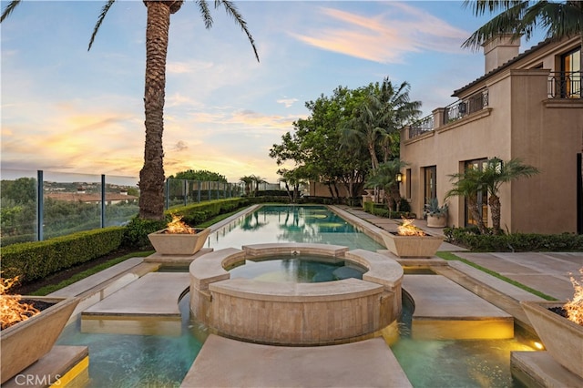 pool at dusk with an in ground hot tub